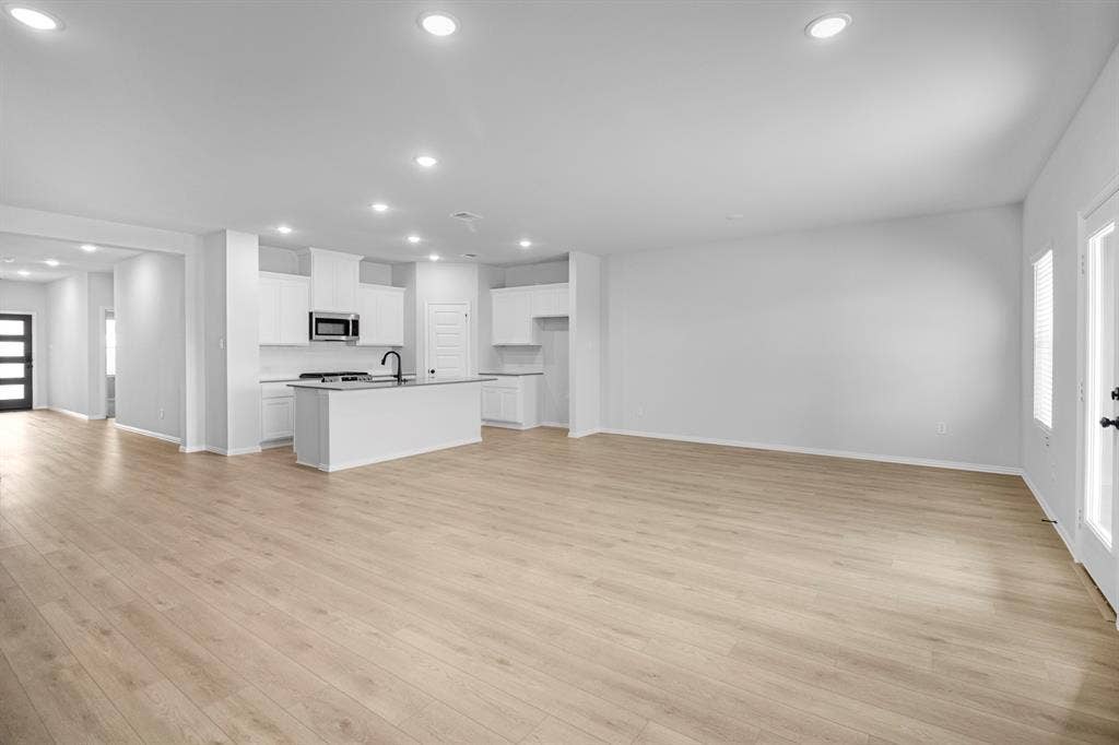 3517 Foxhound Lane, Denton, TX 76208 Open-concept living area featuring wood-finish flooring, recessed lighting, and a kitchen with white cabinetry, stainless steel appliances, and a central island with a sink
