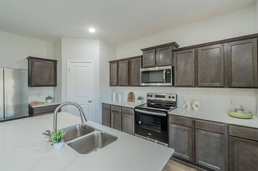 1842 Shady Elm Drive, Lancaster, TX 75146 Kitchen featuring a stainless steel double basin sink, brushed nickel faucet, light-toned countertops, and dark wood-finish cabinetry