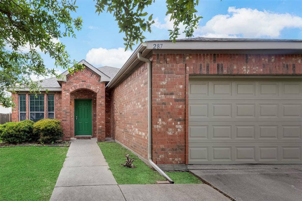 Brick exterior with an arched entryway, a panel garage door, a concrete walkway, and a landscaped front yard