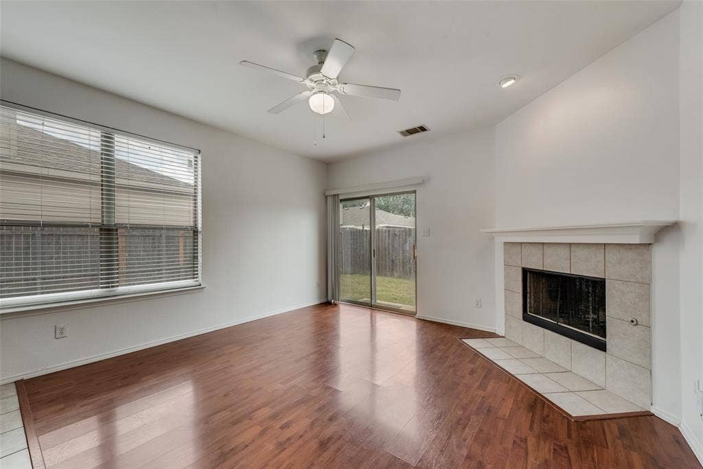 Spacious living area featuring wood-finish flooring, a tiled fireplace with mantel, and a ceiling fan