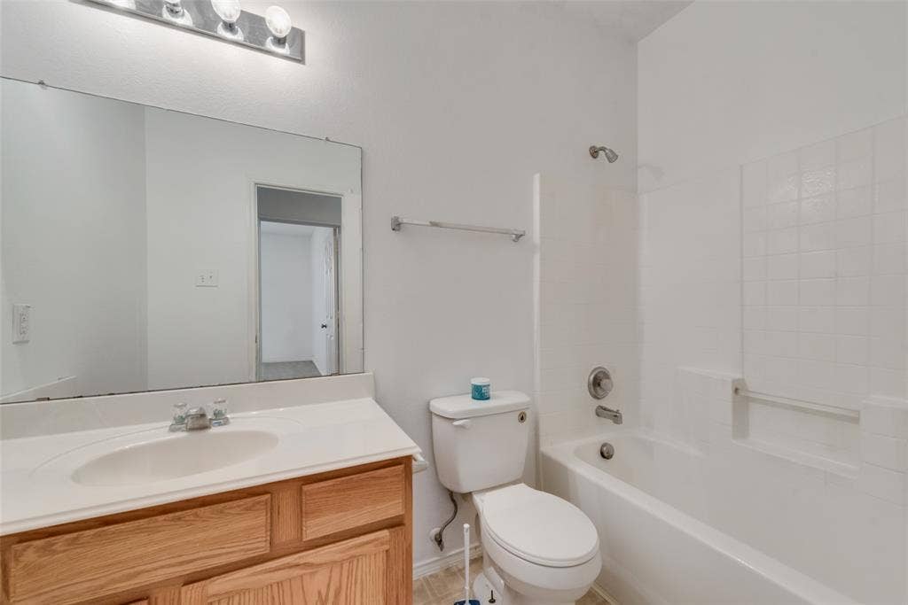 White bathtub with tile surround, wood-finish vanity with a single sink, large wall-mounted mirror, and a chrome light fixture