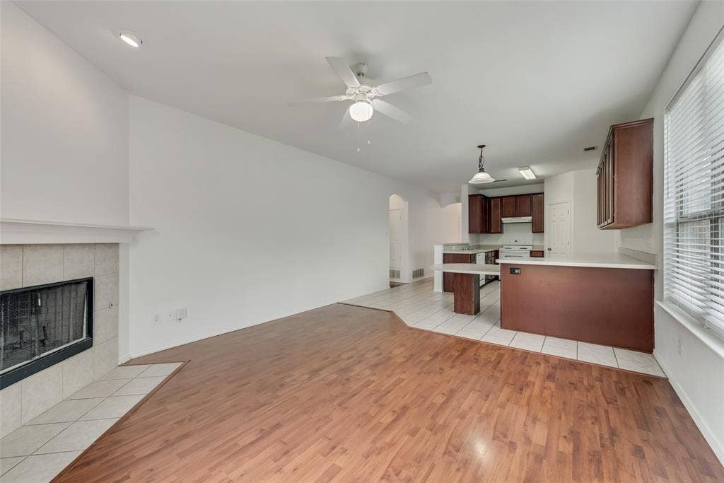 Recessed lighting, ceiling fan, fireplace with tile surround, wood-finish flooring, and a kitchen with dark wood cabinetry
