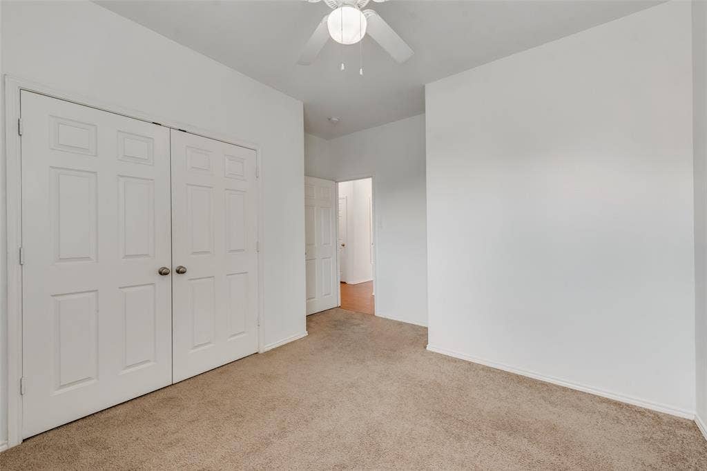 White interior walls, neutral carpet flooring, ceiling fan, and white paneled doors
