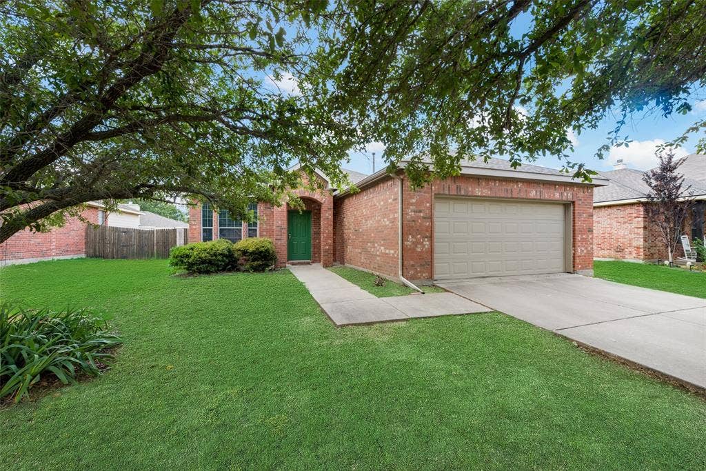 Brick exterior with an attached garage, concrete driveway, and mature landscaping
