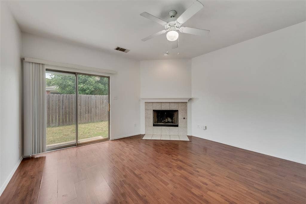 Wood-finish flooring, tiled fireplace surround, ceiling fan, and sliding glass door