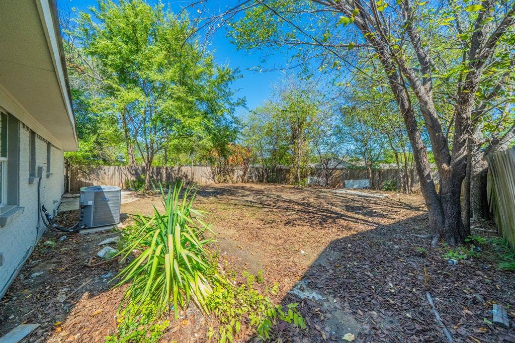 Expansive backyard with a wood privacy fence, mature trees, and a visible exterior air conditioning unit