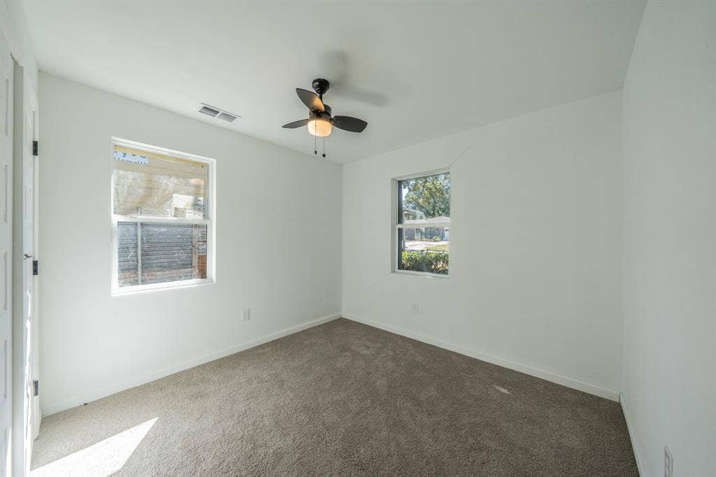 Neutral-toned carpeting, white walls, two windows, and a ceiling fan with integrated lighting