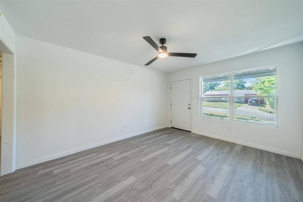 Spacious room with light wood-finish flooring, white walls, and a contemporary ceiling fan with integrated lighting
