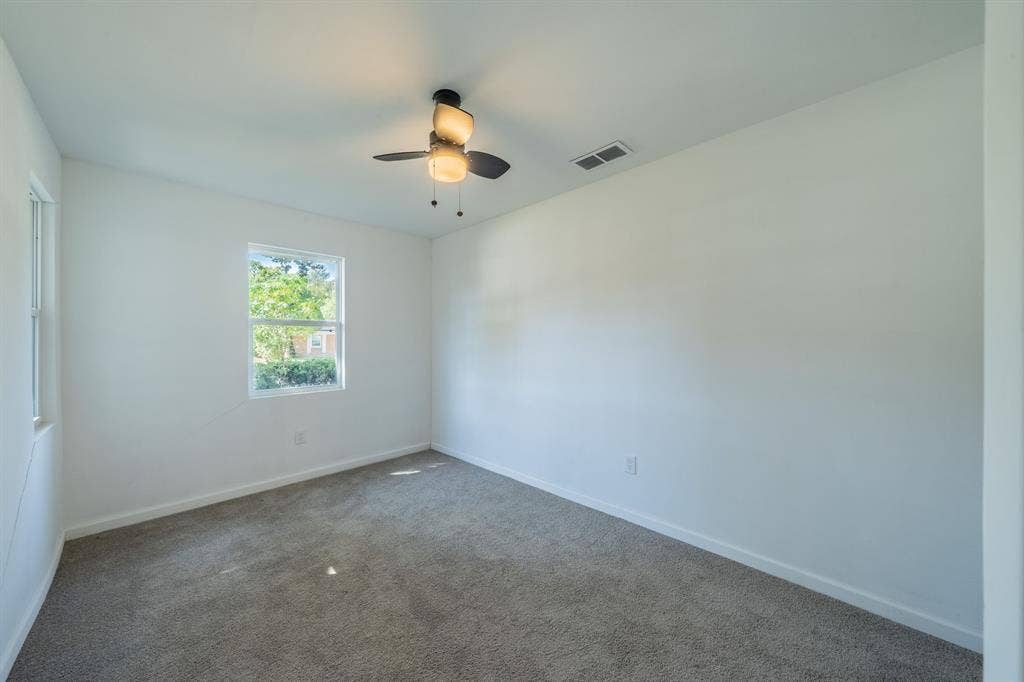 Gray carpeted flooring, white walls, two windows, and a ceiling fan with light fixture