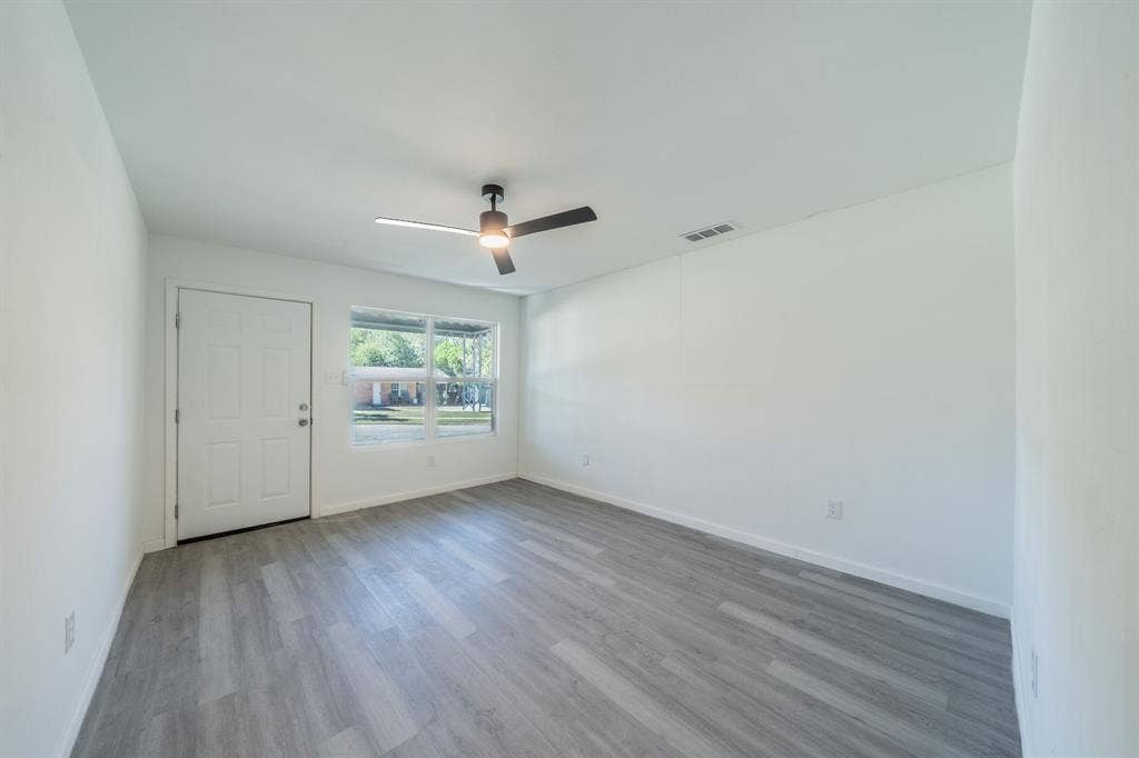 Expansive room featuring wood-finish flooring, a contemporary ceiling fan, and a large window