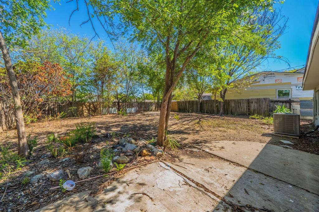 Expansive backyard with a concrete patio, mature trees, and natural landscaping