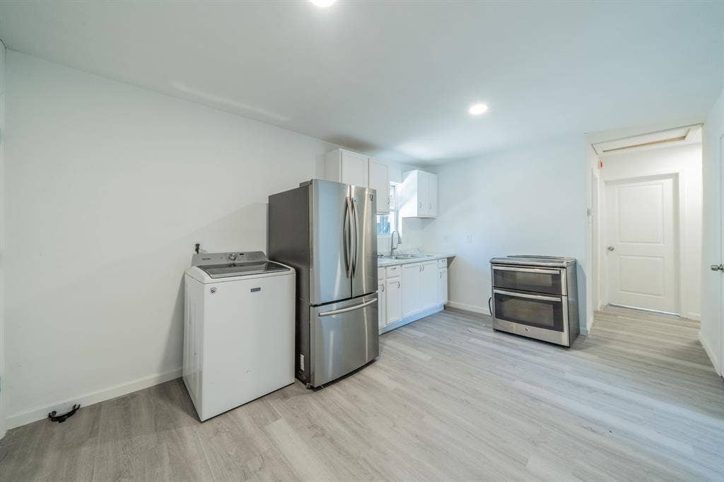 Light wood-finish flooring, white cabinetry, stainless steel refrigerator, and stainless steel range