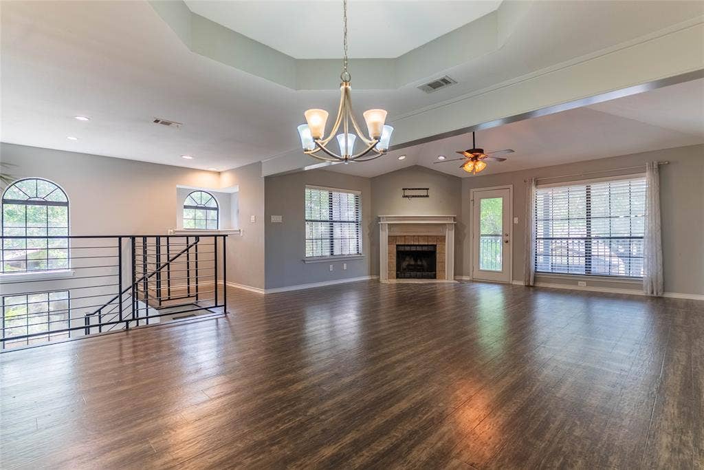 Tray ceiling with recessed lighting, wood-finish flooring, fireplace with mantel, ceiling fan, and staircase with metal railing