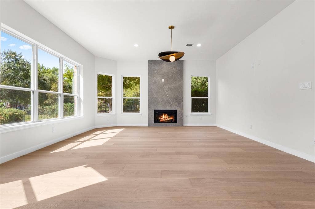 Expansive room featuring wood-finish flooring, a contemporary fireplace with a stone surround, recessed lighting, and multiple windows