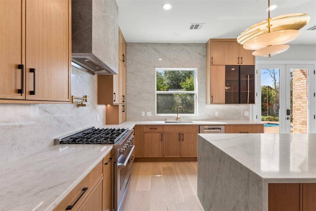 Kitchen featuring wood-finish cabinetry, stainless steel range with pot filler, large center island, and double glass doors opening to the exterior