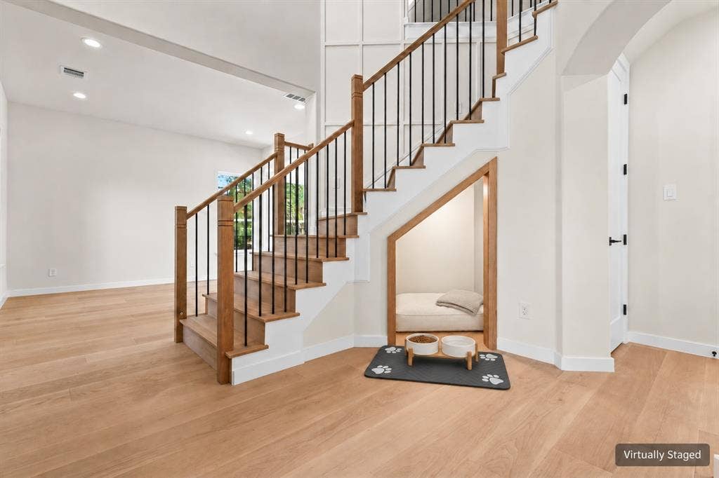 Hardwood staircase with black iron spindles, light wood-finish flooring, recessed lighting, and an arched doorway