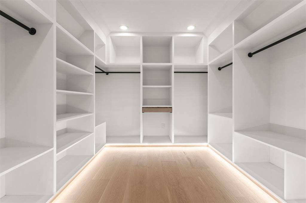 Custom built-in closet system with extensive shelving, hanging rods, recessed lighting, and wood-finish flooring