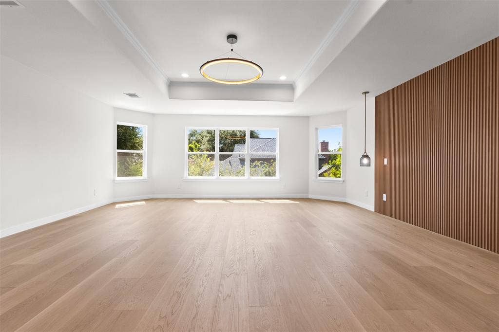 Tray ceiling with recessed lighting, wood-finish flooring, accent wall with vertical wood paneling, multiple windows, and a modern chandelier