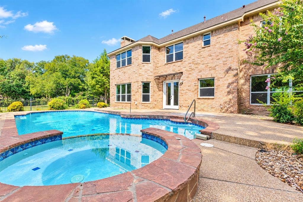Brick exterior with multiple windows, a swimming pool, and an integrated spa