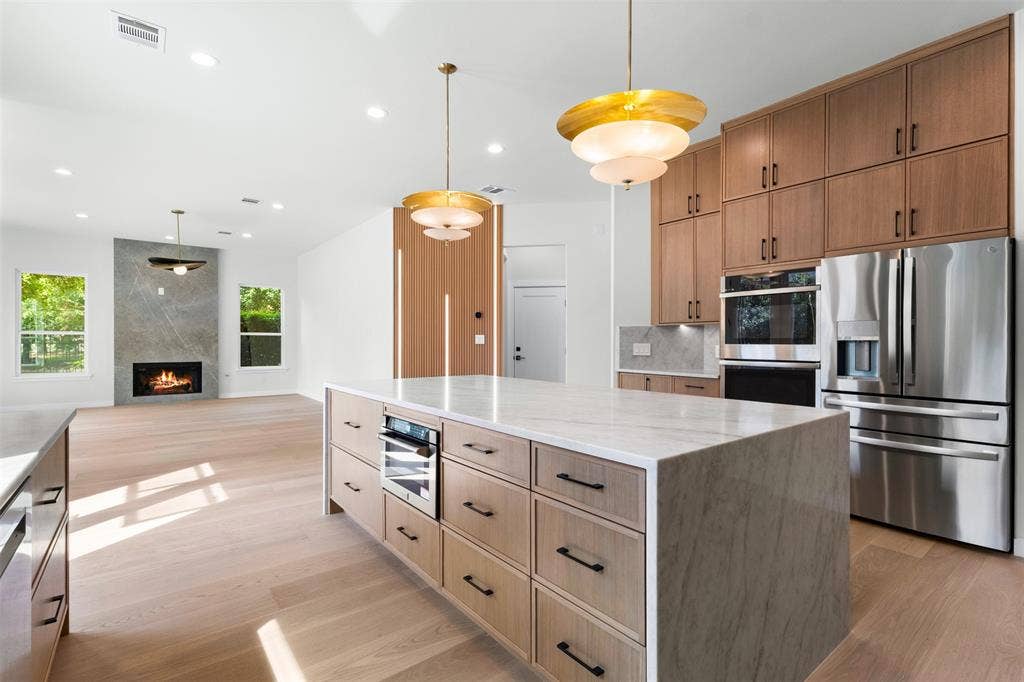 Expansive kitchen island with a stone countertop and integrated wine refrigerator, paired with wood-finish cabinetry and stainless steel appliances