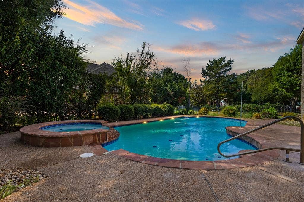 Curved swimming pool with an integrated spa, expansive aggregate concrete decking, and lush perimeter landscaping