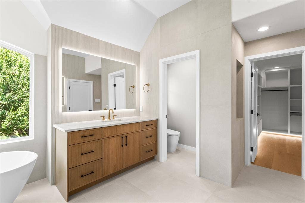 Wood-finish dual vanity with quartz countertop, back-lit mirror, and brass fixtures