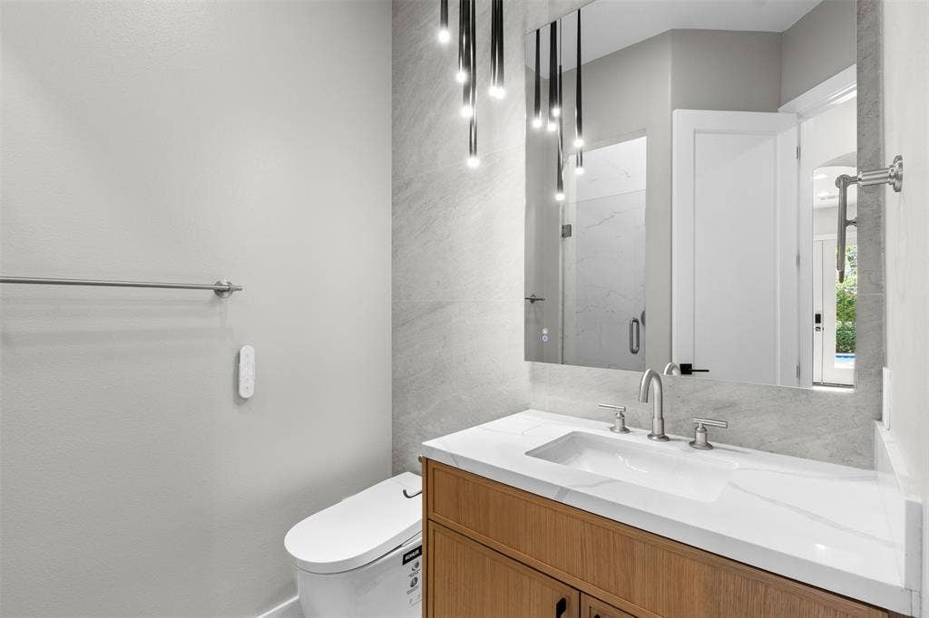 Modern vanity with an integrated rectangular sink, wood-finish cabinetry, contemporary wall-mounted lighting, and a full-width mirror