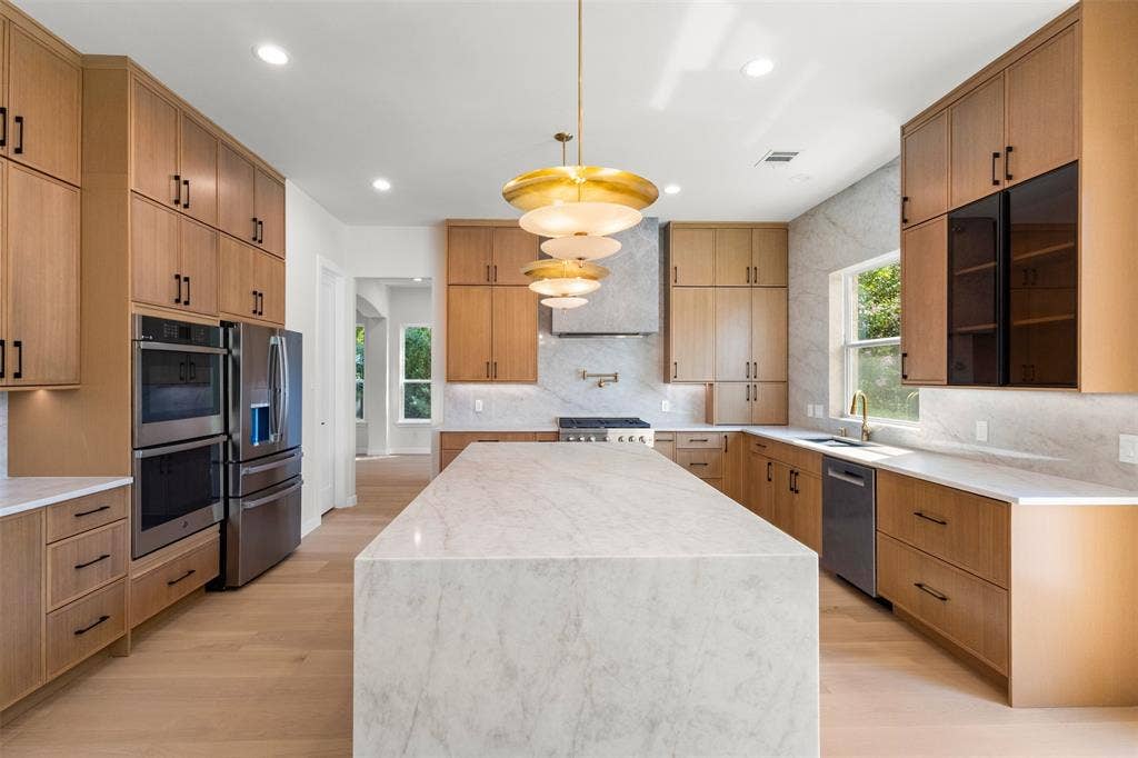 Gourmet kitchen featuring a waterfall island, custom cabinetry, integrated stainless steel appliances, and wood-finish flooring