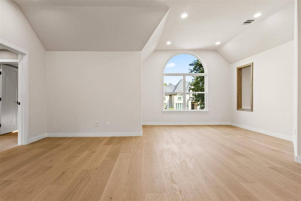 Light wood-finish flooring, vaulted ceiling, arched window, recessed lighting, and a built-in wall niche