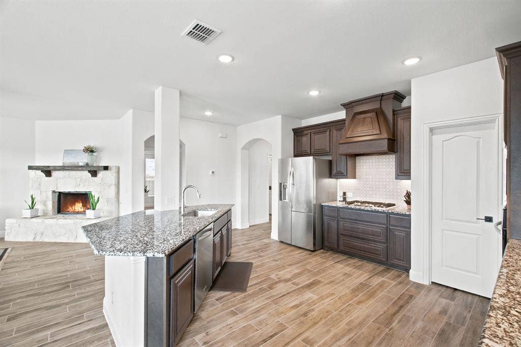 1218 Misty Ridge Drive, Justin, TX 76247 Open-concept design featuring wood-look tile flooring, a kitchen island with stone countertops, stainless steel appliances, and a stone-faced fireplace