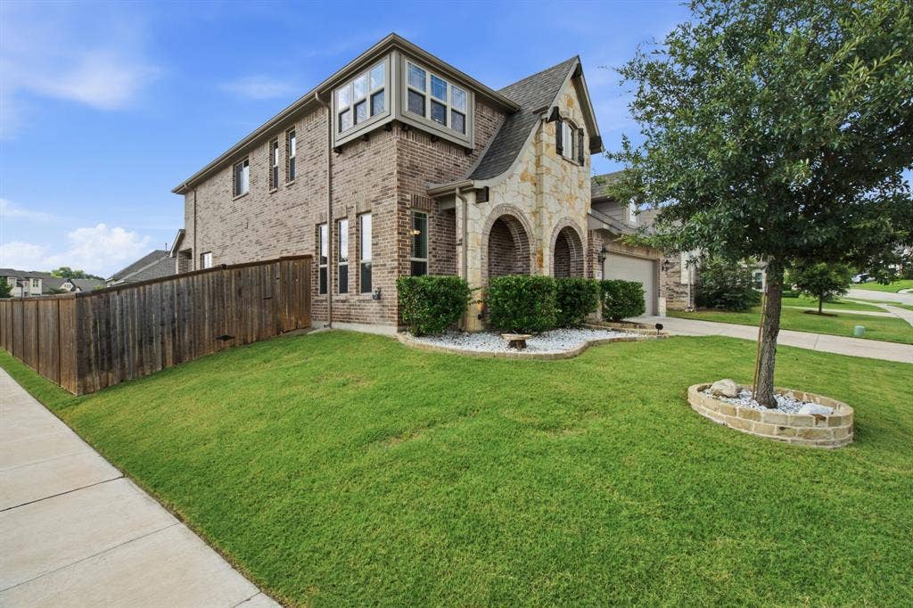 1218 Misty Ridge Drive, Justin, TX 76247 Brick and stone facade, arched entryway, bay window, landscaped front yard with decorative stone beds, and a paved sidewalk