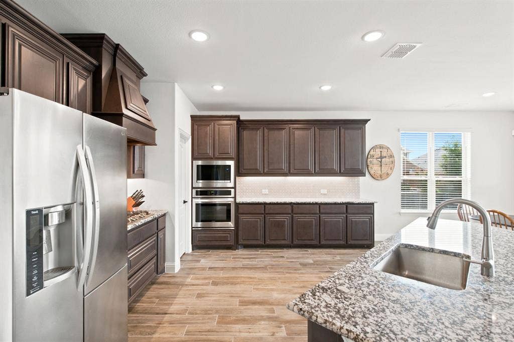 1218 Misty Ridge Drive, Justin, TX 76247 Gourmet kitchen featuring wood-look tile flooring, dark wood cabinetry, stainless steel appliances, speckled stone countertops, and recessed lighting