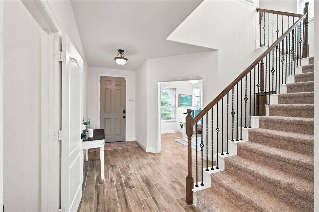 1218 Misty Ridge Drive, Justin, TX 76247 Wood-look tile flooring leading to a staircase with wrought iron balusters and a wood handrail