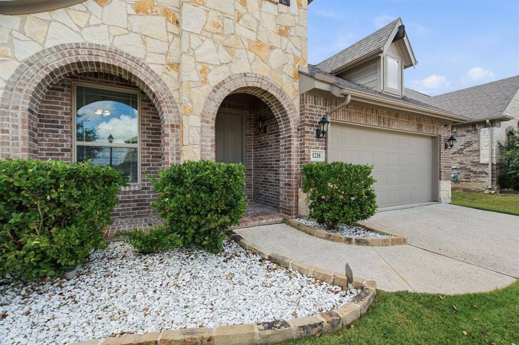 1218 Misty Ridge Drive, Justin, TX 76247 Stone and brick facade with arched entryway, concrete driveway, attached garage, and landscaping with white stone accents