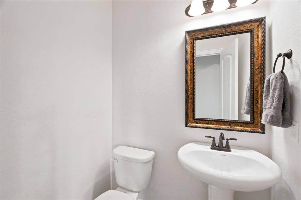 1218 Misty Ridge Drive, Justin, TX 76247 Pedestal sink with dark bronze faucet, framed mirror with ornate detailing, and wall-mounted lighting