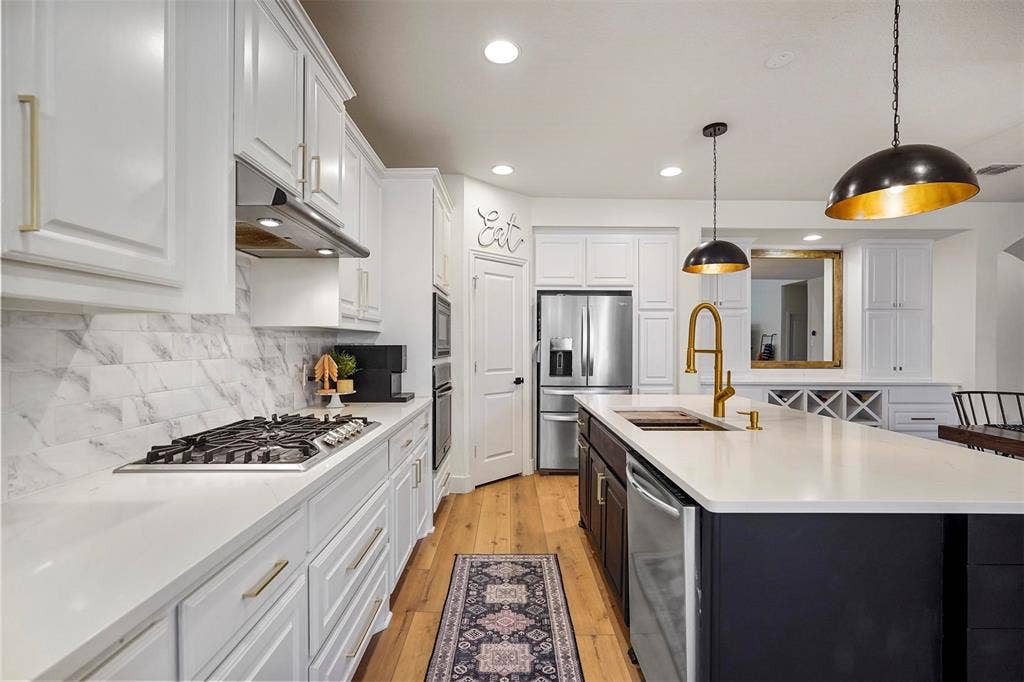 1506 Carnation Street, Celina, TX 75078 White cabinetry with gold-tone hardware, wood-finish flooring, white countertop surfaces, and a built-in stainless steel gas range