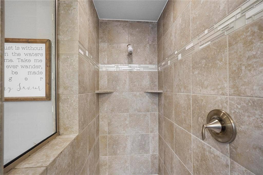 1506 Carnation Street, Celina, TX 75078 Tiled shower with decorative accent banding, built-in shelving, and a brushed nickel shower fixture
