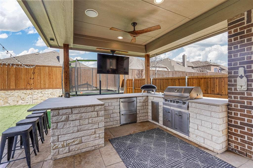1506 Carnation Street, Celina, TX 75078 Covered patio featuring an outdoor kitchen with built-in grill, stone veneer construction, and integrated ceiling fan