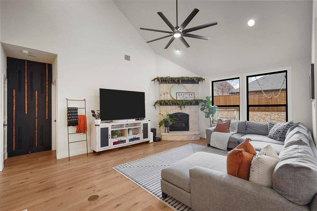 1506 Carnation Street, Celina, TX 75078 Vaulted ceiling with a ceiling fan, light wood-finish flooring, corner fireplace with a stone surround, black-framed windows, and built-in recessed lighting