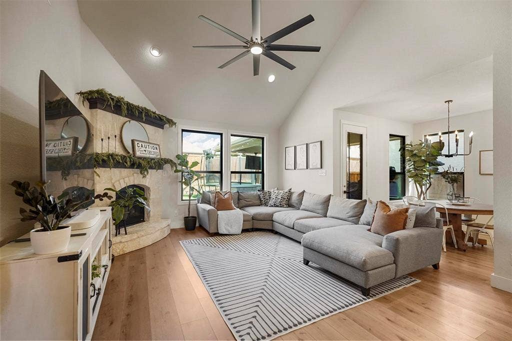1506 Carnation Street, Celina, TX 75078 Vaulted ceiling with an integrated ceiling fan, stone-clad fireplace, large windows with black frames, and wide plank wood-finish flooring