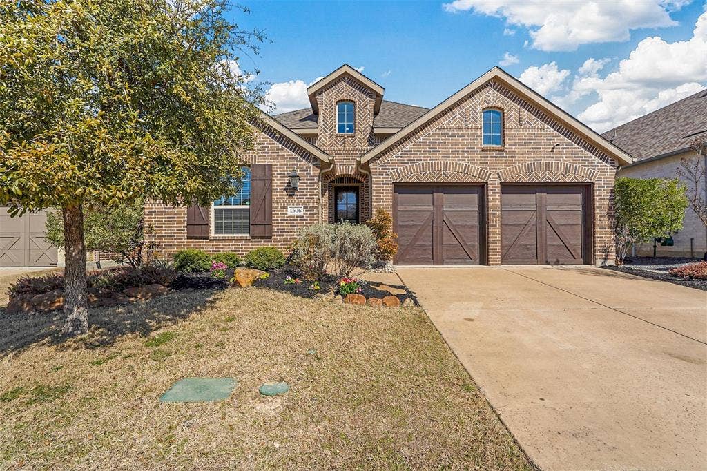 1506 Carnation Street, Celina, TX 75078 Brick facade with decorative arched lintels, two-car garage with wood-finish doors, landscaped front yard, and a concrete driveway