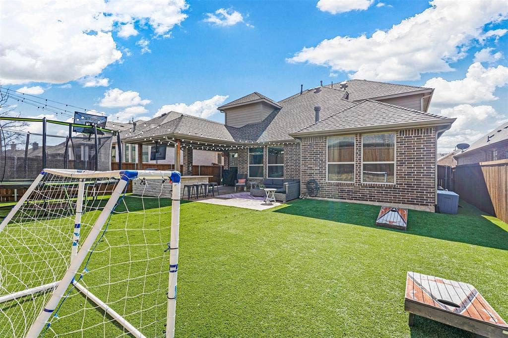 1506 Carnation Street, Celina, TX 75078 Expansive artificial turf backyard featuring a covered patio with string lights, a built-in bar, and a brick exterior