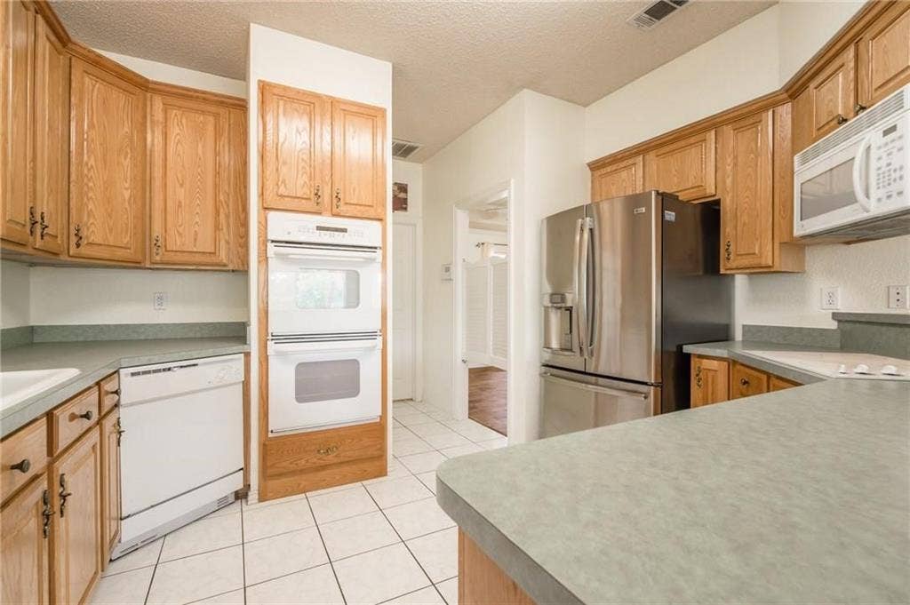 5000 Pointclear Court, Arlington, TX 76017 Kitchen featuring wood cabinetry, white tile flooring, stainless steel refrigerator, white built-in double oven, and a white dishwasher