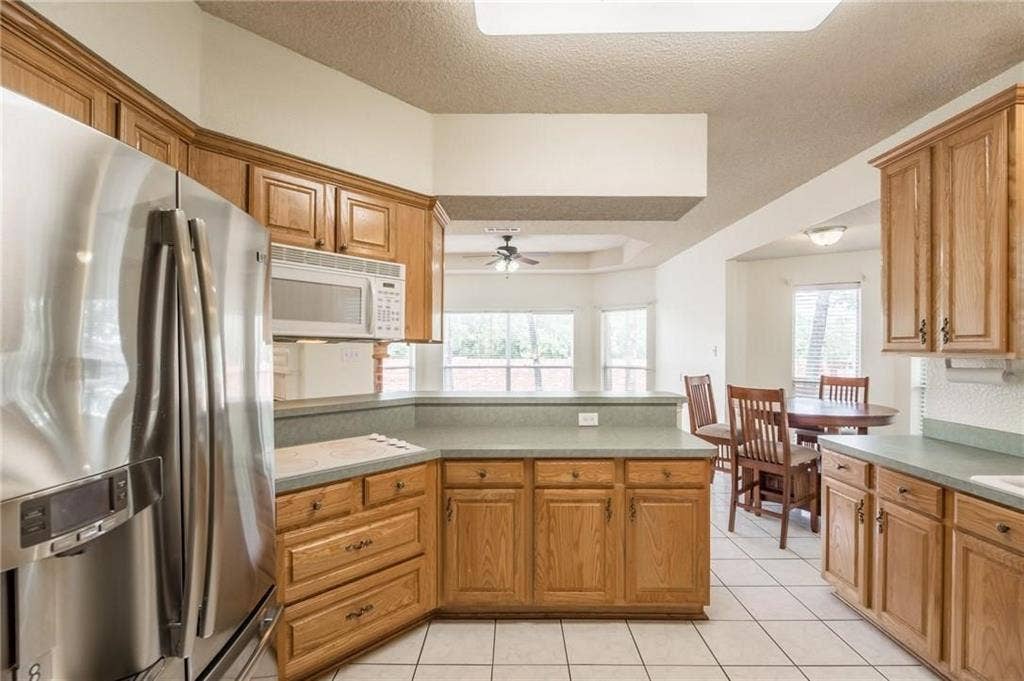 5000 Pointclear Court, Arlington, TX 76017 Kitchen featuring wood cabinetry, stainless steel refrigerator, built-in microwave, light-toned countertops, and tile flooring