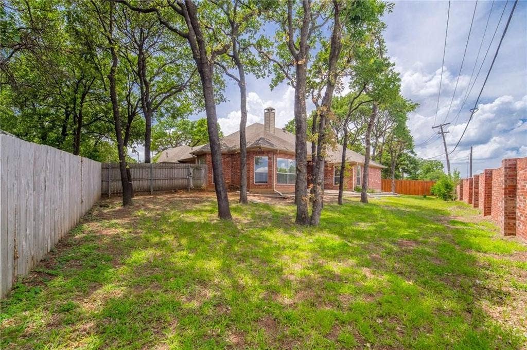 5000 Pointclear Court, Arlington, TX 76017 Expansive backyard featuring a manicured lawn, mature trees, and a wooden privacy fence