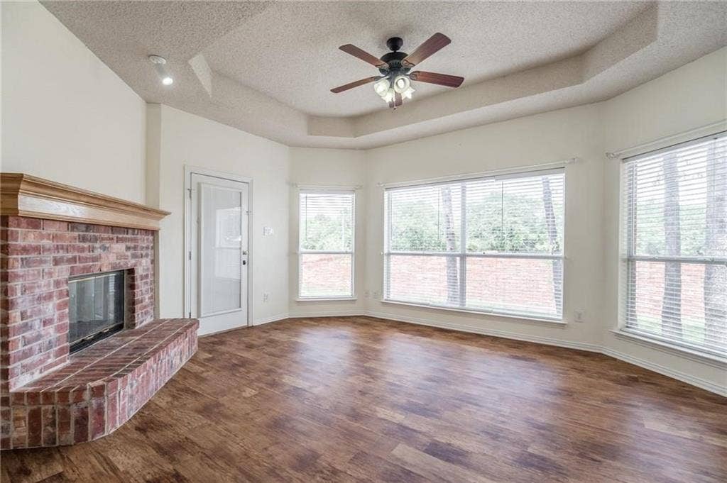 5000 Pointclear Court, Arlington, TX 76017 Wood-finish flooring throughout, brick fireplace with wood mantel, multiple windows with blinds, tray ceiling, and ceiling fan with integrated lighting