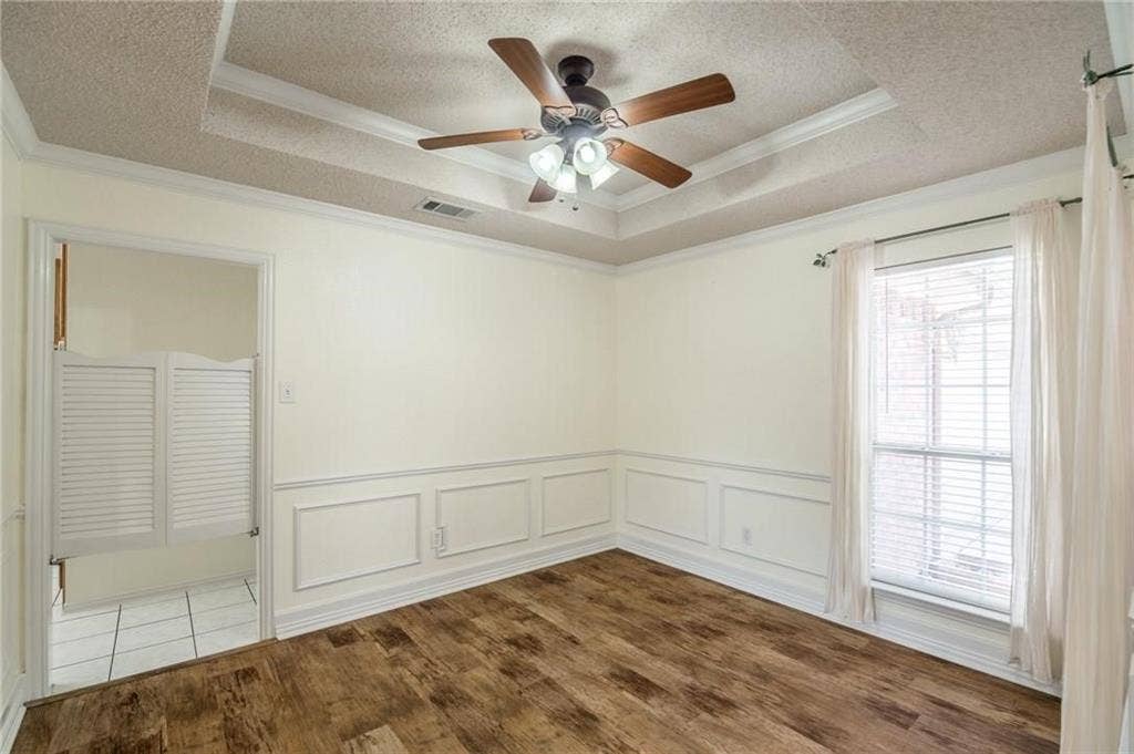 5000 Pointclear Court, Arlington, TX 76017 Wood-finish flooring, accent wall paneling, a tray ceiling with a built-in ceiling fan, and a window with blinds