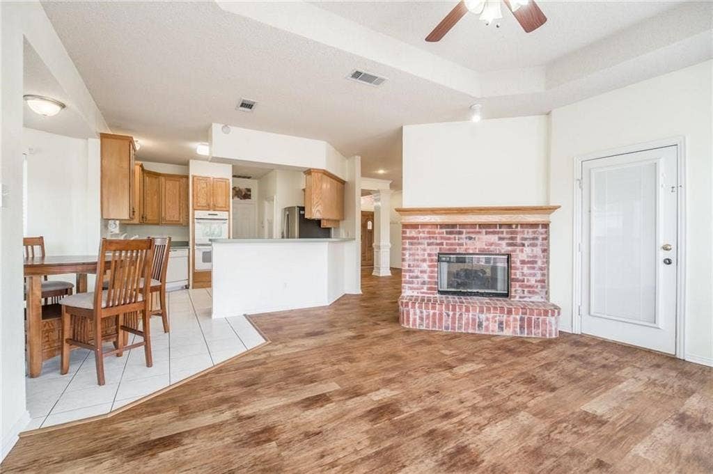 5000 Pointclear Court, Arlington, TX 76017 Tray ceiling with a ceiling fan, brick fireplace with a wood mantel, wood-finish flooring, and a kitchen with wood cabinetry