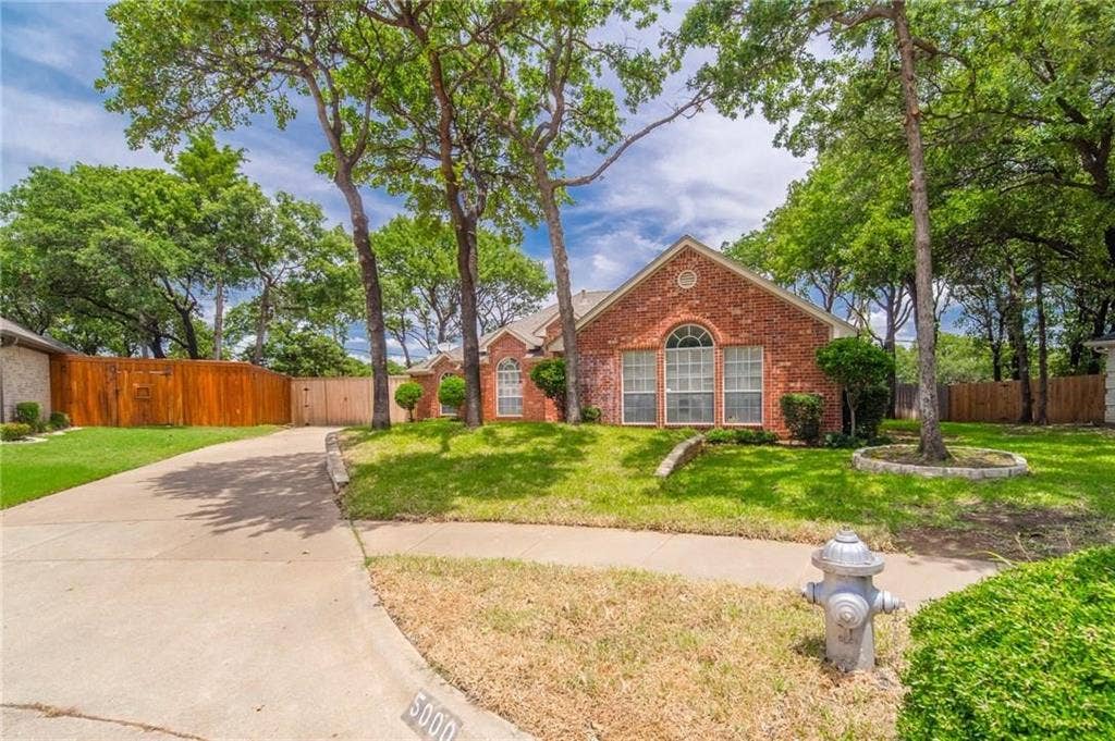 5000 Pointclear Court, Arlington, TX 76017 Brick exterior with an arched window, concrete driveway, and mature trees
