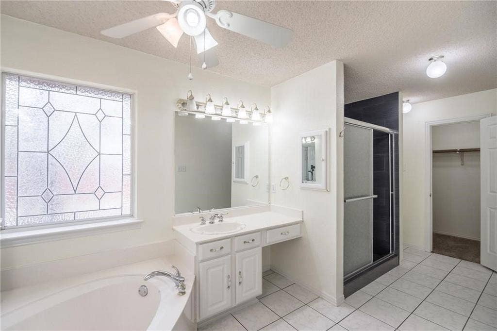 5000 Pointclear Court, Arlington, TX 76017 Bathroom featuring a built-in tub, white vanity with integrated sink, glass-enclosed shower, decorative privacy window, and ceiling fan